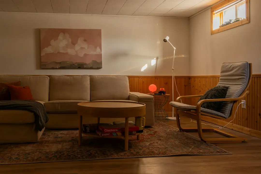 A cozy living room with a beige sectional sofa, a round wooden coffee table, a floor lamp and an armchair